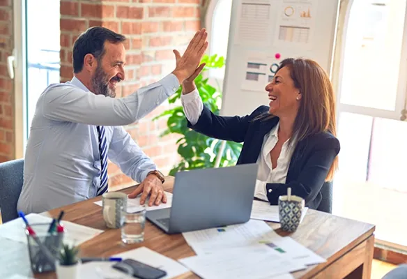 Two business partners high-fiving at a desk